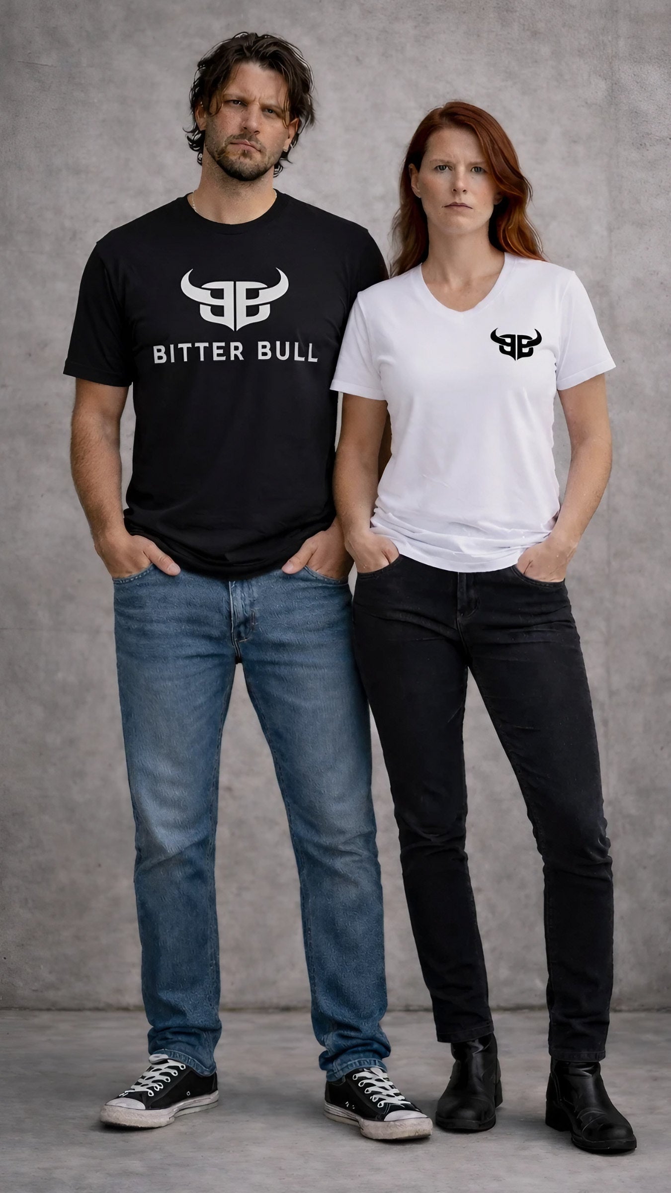 Man and woman wearing Bitter Bull graphic t-shirts in black and white, standing against a raw concrete wall in a minimal streetwear style